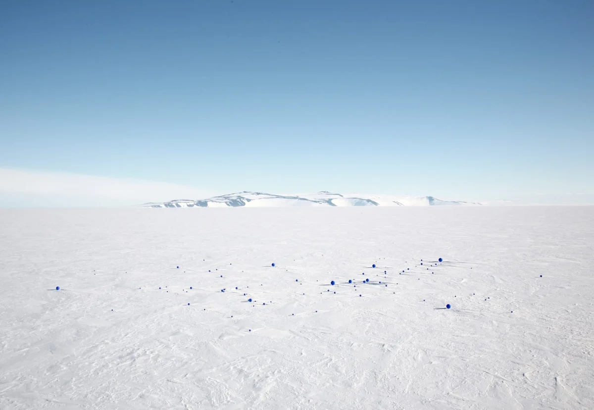 A bright Antarctic expanse with small black spheres on the ground
