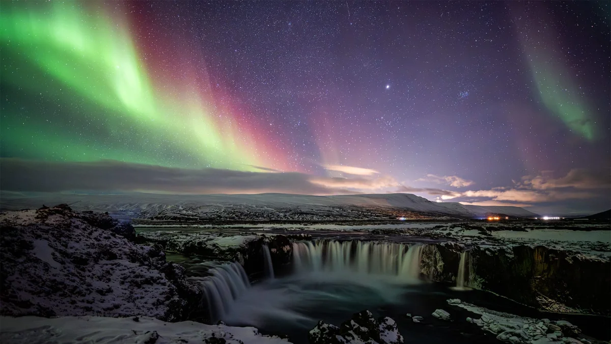 a photograph of aurora borealis over a waterfall in Iceland