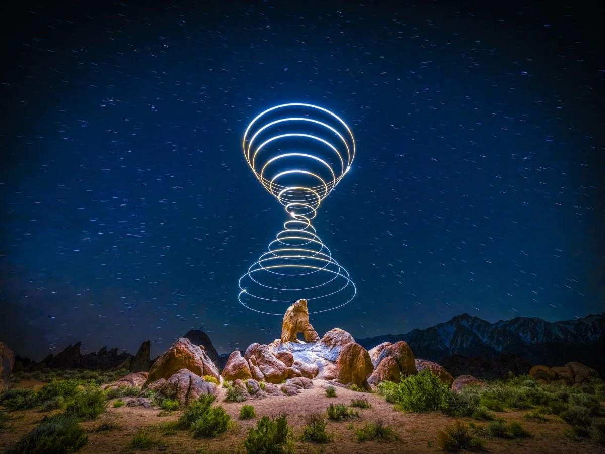 a "light painting" photograph with a double cone of swirling light, created using a drone, over a dramatically lit nighttime desert landscape