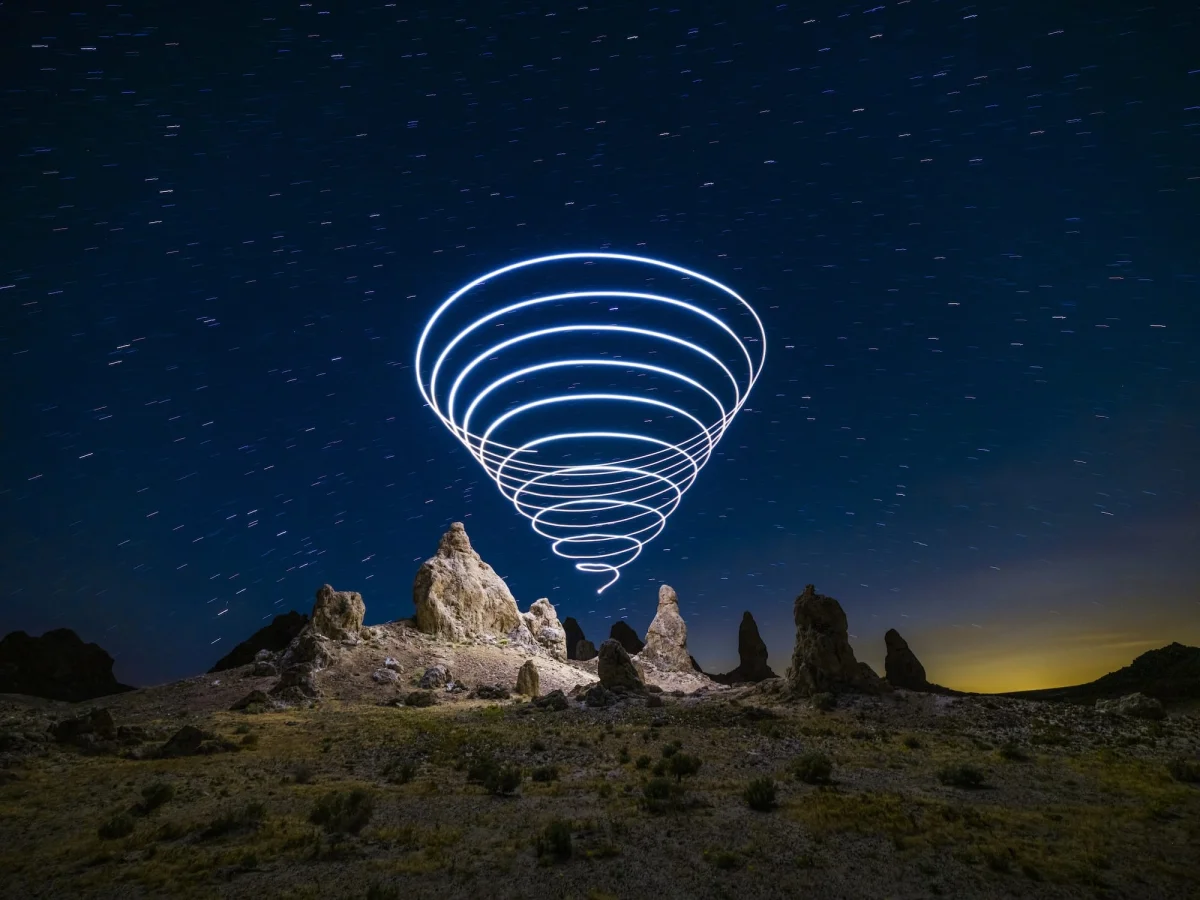 a "light painting" photograph with a cone of swirling light, created using a drone, over a dramatically lit nighttime desert landscape