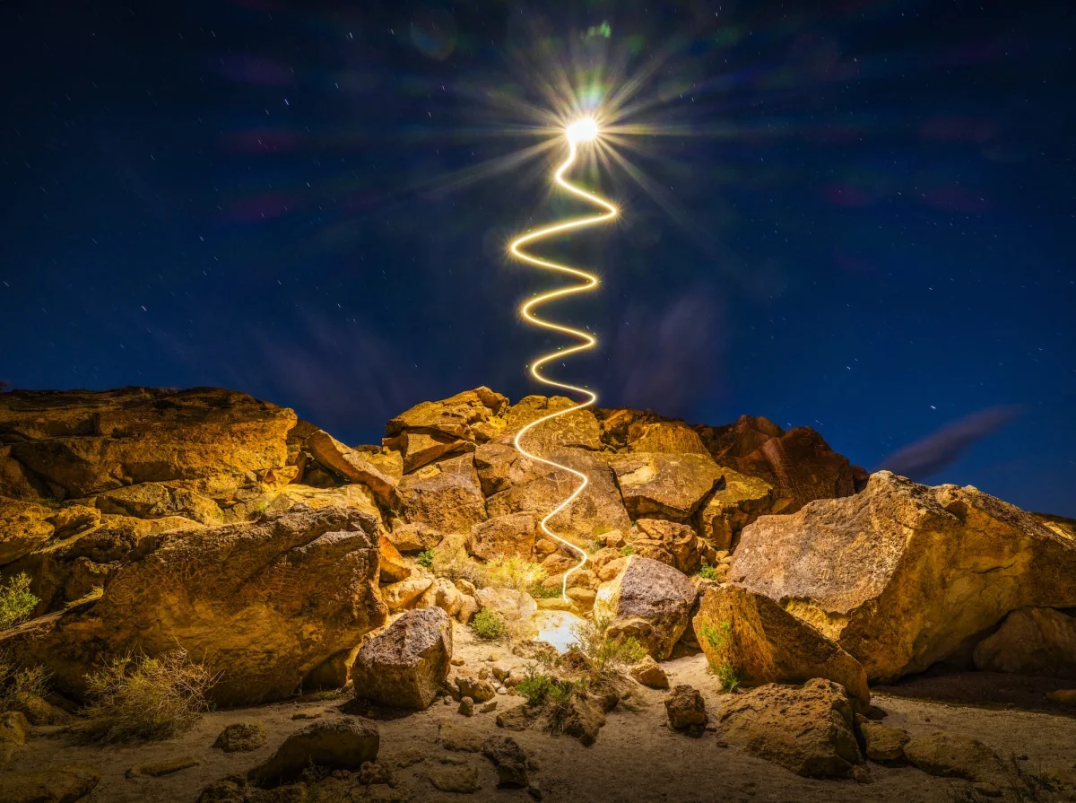 a "light painting" photograph with a squiggle of light, created using a drone, over a dramatically lit nighttime desert landscape